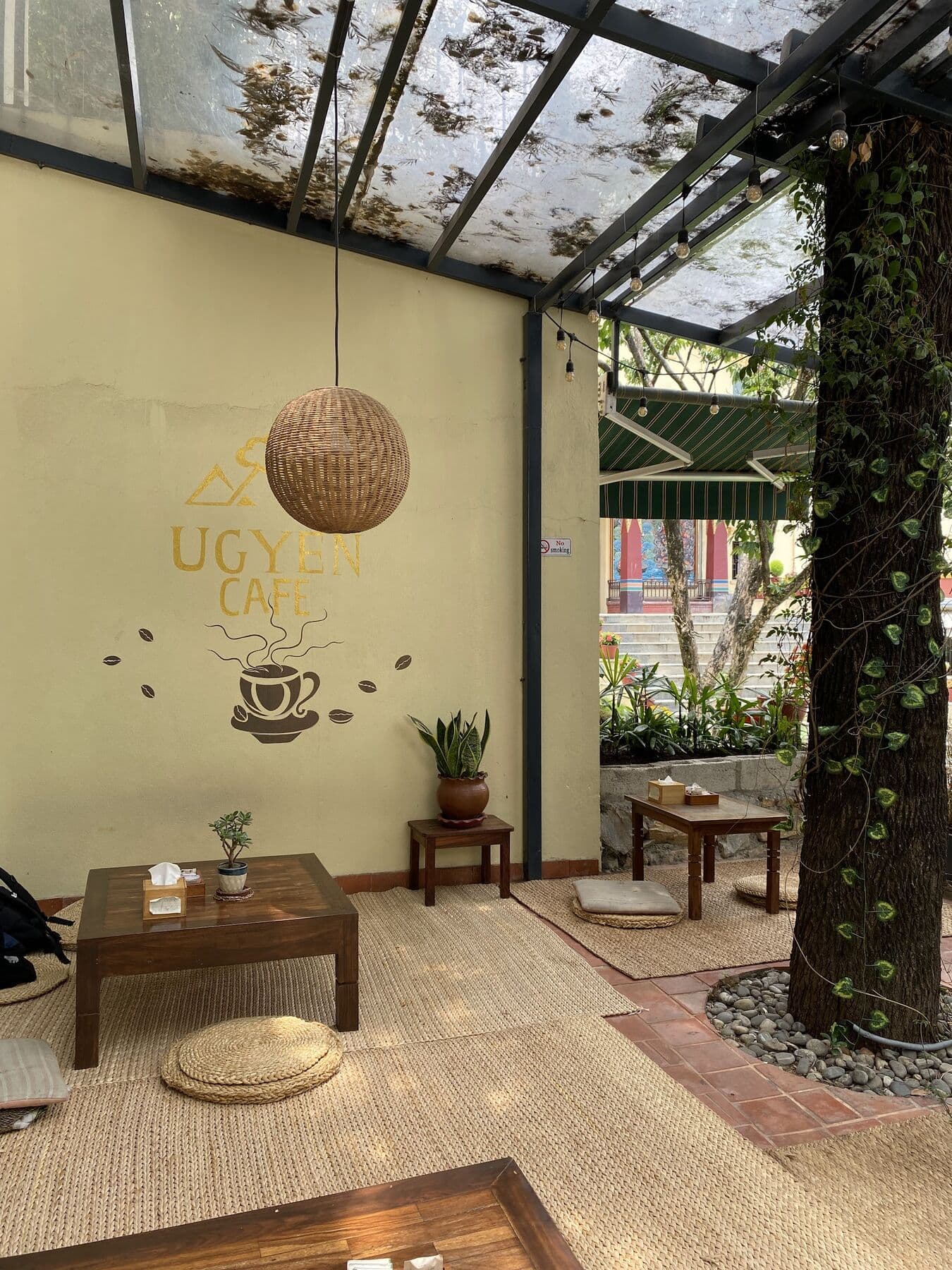 Low tables and floor cushions on a jute rug beside an ivy-covered tree trunk