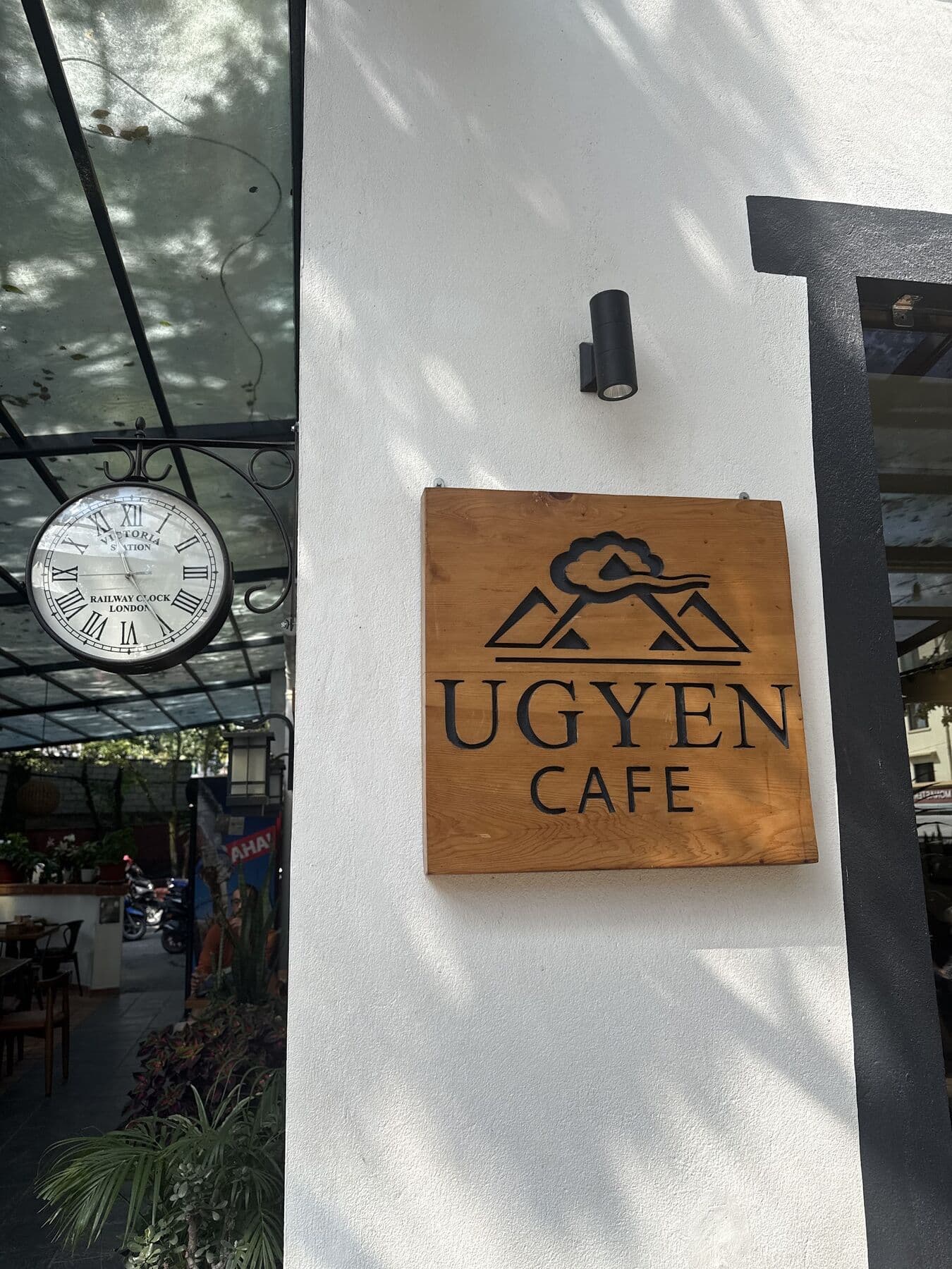 The carved wooden Ugyen Cafe sign on a white wall beside a clock