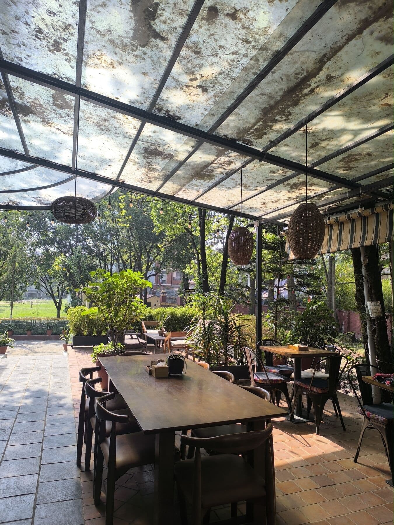 The empty terrace: a long wooden table under a glass roof, trees beyond